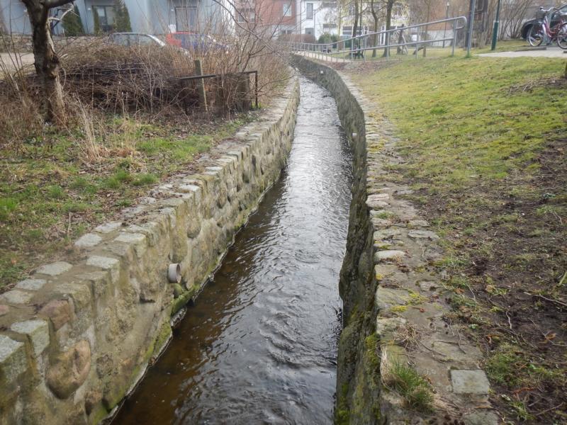 Fotos vom Amtsbach. Die Ufer sind wie ein Kanal ausgebaut. Der Bach fließt durch einen Ort.
