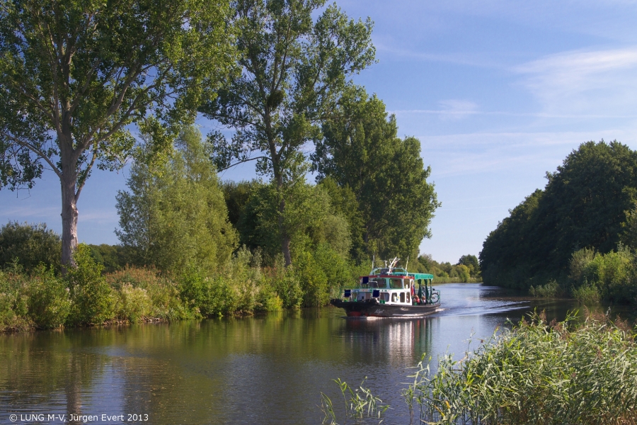 Auf einem Foto ist ein Bereich der Störwasserstraße zu sehen. Entlang des Gewässers stehen Bäume und Sträucher. Auf dem Wasser fährt ein Boot.